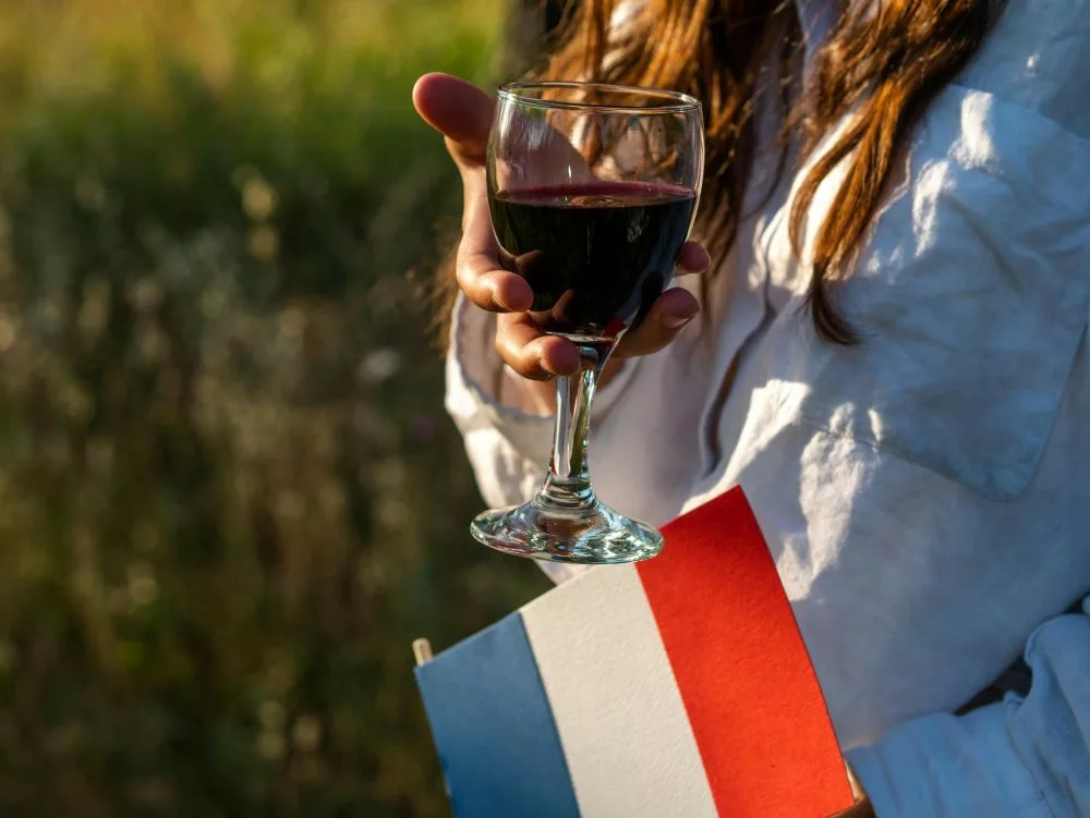 une femme tient un verre de vin rouge à main et un drapeau français de l'autre